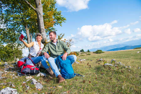 Young couple drinking water while resting on the rock during the travel in the mountainsの写真素材