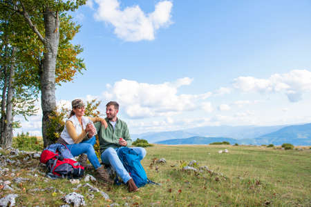 Young couple drinking water while resting on the rock during the travel in the mountainsの写真素材