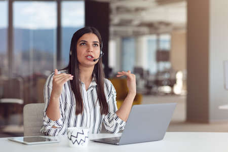 Portrait of focused woman in headphones taking part in webinar in officeの写真素材