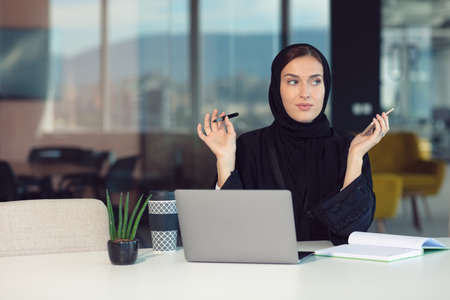 Pensive arabic businesswoman sitting at workplace in officeの写真素材