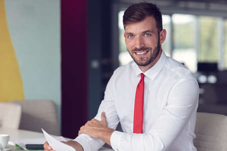 Portrait of young man sitting at his desk in the officeの写真素材