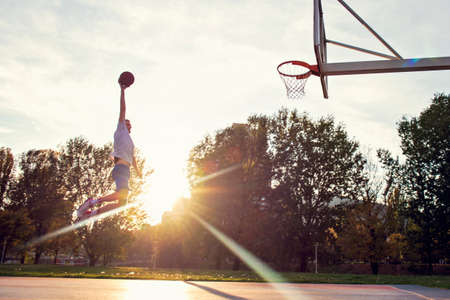 Young man jumping and making a fantastic slam dunk playing streetball, basketball. Urban authentic.の写真素材