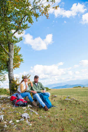 Young couple drinking water while resting on the rock during the travel in the mountainsの写真素材