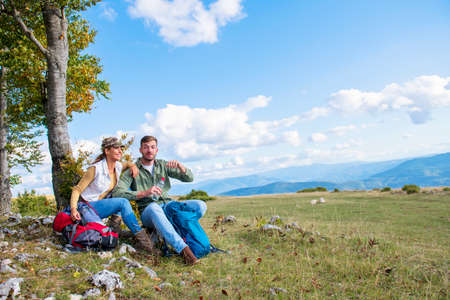 Young couple drinking water while resting on the rock during the travel in the mountainsの写真素材