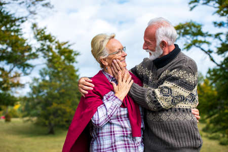 Elderly couple embracing in autumn park. Enjoying in love.の写真素材