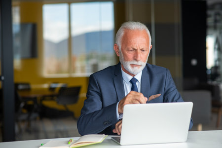 Handsome smiling senior man while sitting at his cozy workplace with laptop at home, retired male chatting with friends in social media,の写真素材