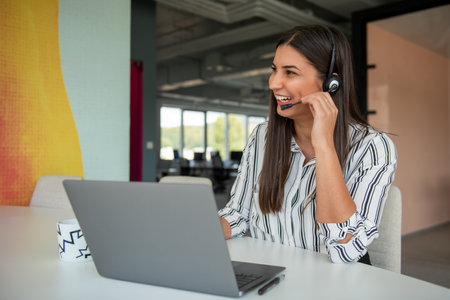 Brunette Lady Video Calling On Laptop Wearing Headphones Smiling And Waving Hand To Webcam Communicating Onlineの写真素材