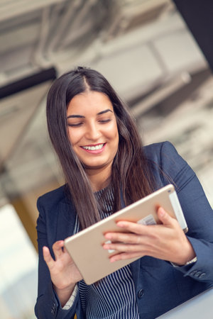 Young attractive female manager working on digital tablet while standing in modern officeの写真素材
