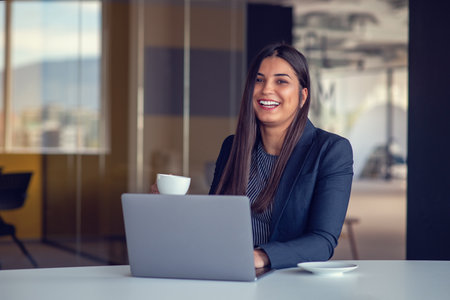 Young woman working on laptop and drinking coffee in officeの写真素材