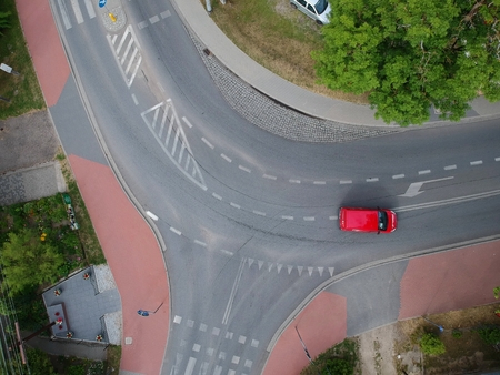 Red car driving across curved intersection in city, aerial view.