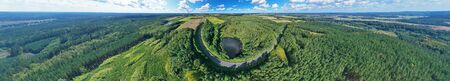 Aerial drone wide panoramic view on wind turbine, snake shape road, wheat fields and forest during...