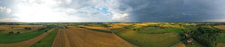 Aerial drone wide panoramic view on agricultural landscape with wheat field, village, meadows, forest and rain storm on horizonの写真素材