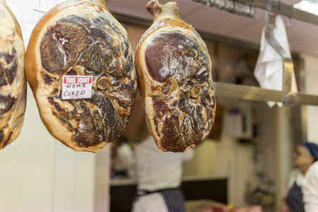 Choice and premium home cured pork joints hanging in a butchers shop on a market stall in England, United Kingdomの写真素材