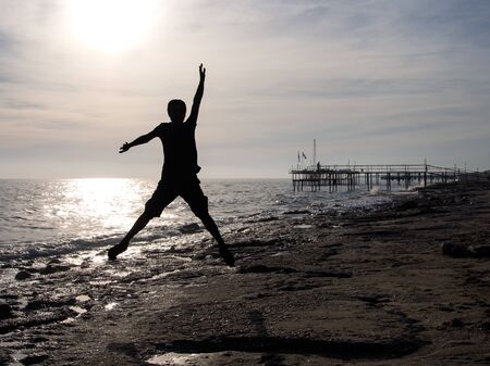 Young man in a jump on the sea beach at sunset.の写真素材