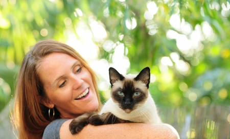 Pretty woman with red hair holding Siamese cat outdoorsの写真素材