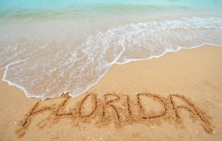 A warm tropical beach with blue water and waves and Florida written in the sandの写真素材