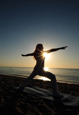 Woman doing Warrior II yoga pose on beach during a beautiful sunriseの写真素材