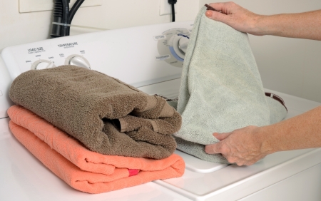 woman doing laundry and folding clean towels near washer and dryerの写真素材
