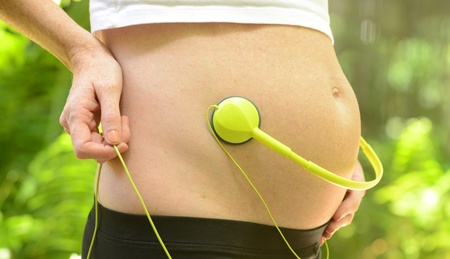 woman playing music for unborn baby with headphones on stomach during pregnancy
