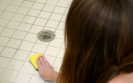 woman scrubbing shower tiles with scour pad to clean soap scumの写真素材