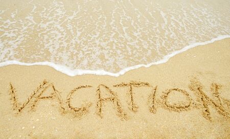 A warm tropical beach with waves and vacation written in the sand の写真素材