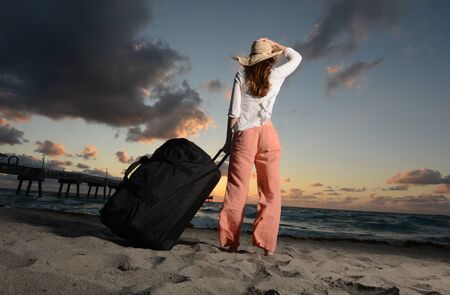 Woman holding hat on head while looking at the ocean during sunset on vacationの写真素材