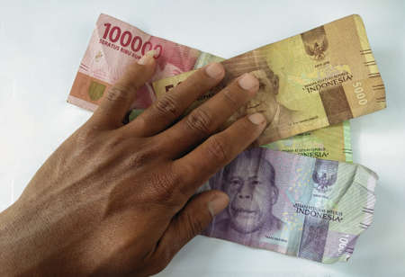 Human Asian man hand holding Indonesian paper money on white background.Brown skin color man hand...