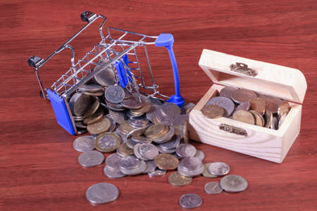 Miniature shopping cart full of coins on a wooden background- payments, investments and commerce conceptの写真素材