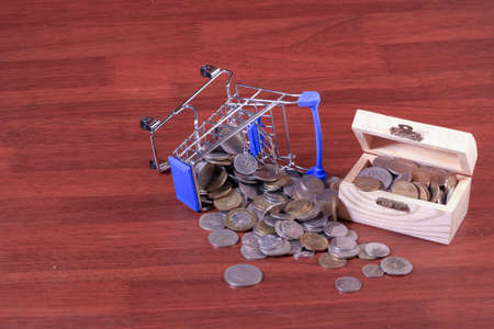 Miniature shopping cart full of coins on a wooden background- payments, investments and commerce conceptの写真素材