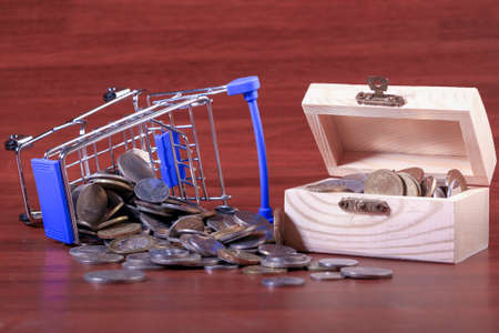 Miniature shopping cart full of coins on a wooden background- payments, investments and commerce conceptの写真素材