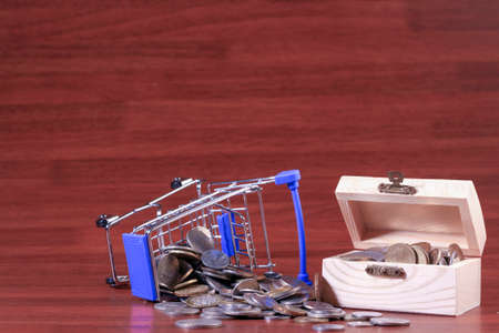 Miniature shopping cart full of coins on a wooden background- payments, investments and commerce conceptの写真素材