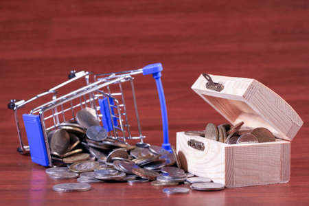 Miniature shopping cart full of coins on a wooden background- payments, investments and commerce conceptの写真素材