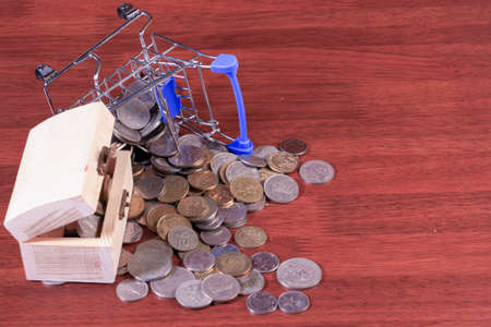 Miniature shopping cart full of coins on a wooden background- payments, investments and commerce conceptの写真素材