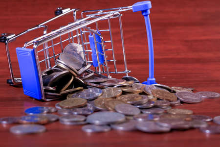 Miniature shopping cart full of coins on a wooden background- payments, investments and commerce conceptの写真素材