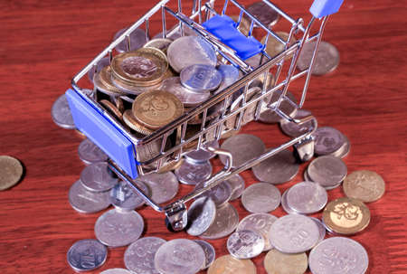 Miniature shopping cart full of coins on a wooden background- payments, investments and commerce conceptの写真素材