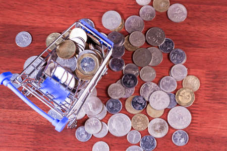 Miniature shopping cart full of coins on a wooden background- payments, investments and commerce conceptの写真素材