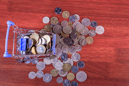 Miniature shopping cart full of coins on a wooden background- payments, investments and commerce conceptの写真素材