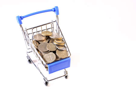 Miniature shopping cart full of coins on a wooden background- payments, investments and commerce conceptの写真素材