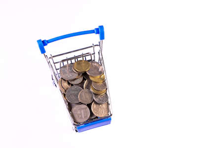 Miniature shopping cart full of coins on a wooden background- payments, investments and commerce conceptの写真素材