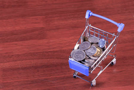 Miniature shopping cart full of coins on a wooden background- payments, investments and commerce conceptの写真素材