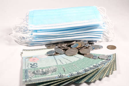 rice gouging during shortage of virus masks. High price of masks and demand during quarantine in Malaysia and global pandemic. Pile of anti virus surgical face masks and money. financing Concept.の写真素材