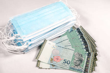 rice gouging during shortage of virus masks. High price of masks and demand during quarantine in Malaysia and global pandemic. Pile of anti virus surgical face masks and money. financing Concept.の写真素材