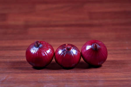 Red onions isolated on wooden background. Red onions are cultivars of the onion with purplish-red skin and white flesh tinged with red. They are most commonly used in the culinary arts,の写真素材