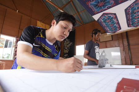 Kedah, MALAYSIA - Aug 13 2020 : Unidentified local woman/ men sketching freehand with canting tools and hot wax to create a traditional Batik Canting at workshop.のeditorial素材