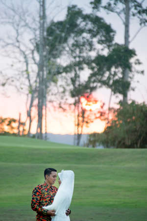 creative outdoor photo shoot of a malay loving couple bride and groom on their wedding wearing a traditional malay dress and camouflage dressの写真素材