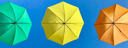 View of 3 colored umbrellas under blue background.