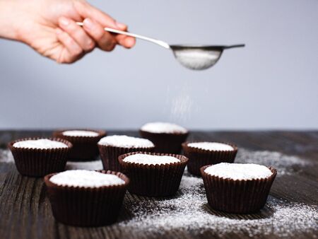 Chocolate cupcakes sprinkled with powdered sugar and handの写真素材