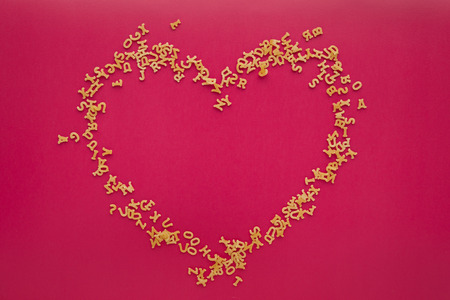 Heart from alphabet pasta on pink backgroundの写真素材