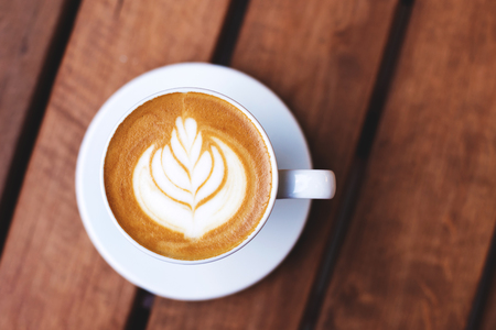 A cup of coffee with latte art on wooden table.の写真素材