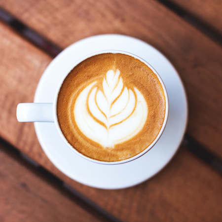 A cup of coffee with latte art on wooden table.の写真素材